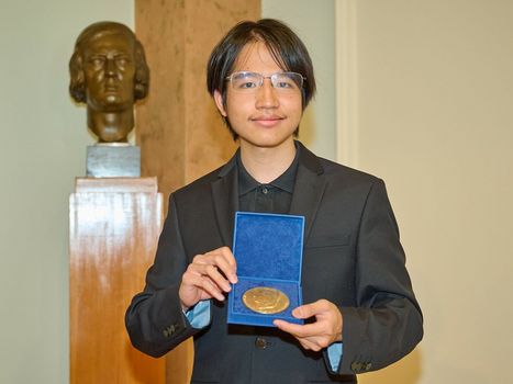 Junger Mann hält eine Goldmedaille neben einer Schumann-Bronzebüste 