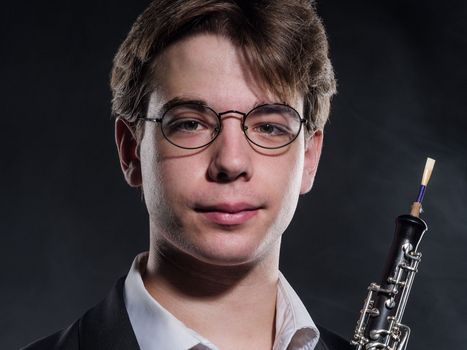 Junger Mann mit Brille und Oboe vor schwarzem Hintergrund